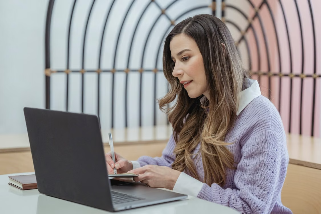 Woman writing plans in a notebook while working beside her laptop