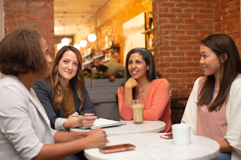 Four women discussing plans around a café table with notebooks and drinks
