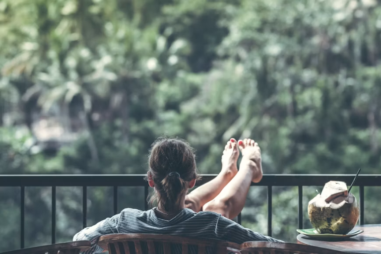 Person relaxing in a chair overlooking trees with a coconut drink nearby