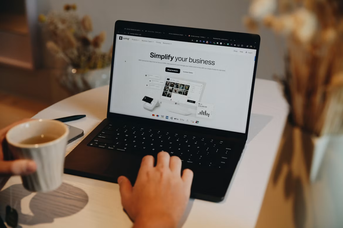 Person browsing a business website on a laptop while holding a coffee mug