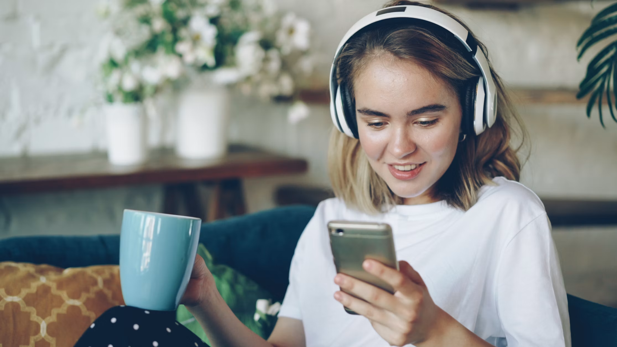Woman relaxing at home with headphones, a warm drink, and her phone