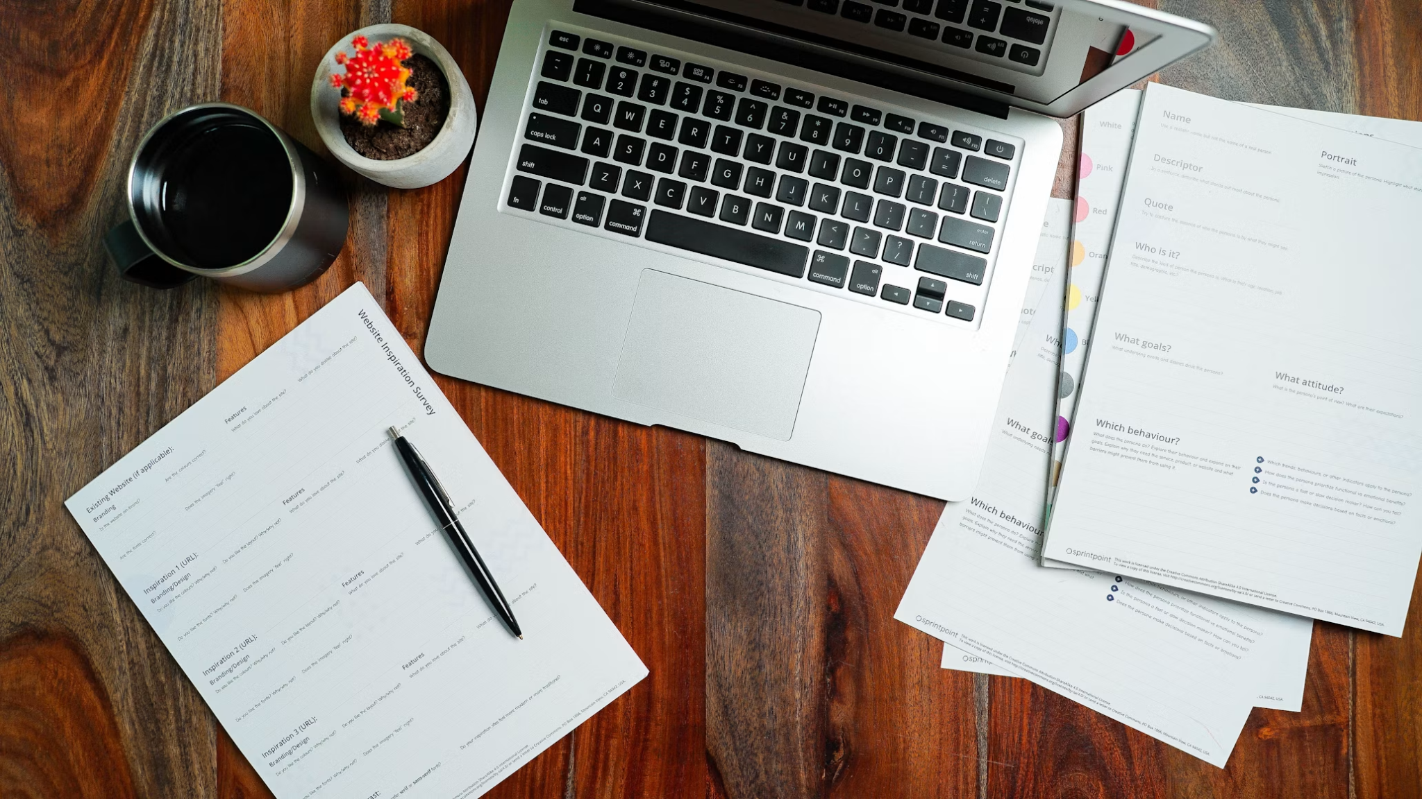 Laptop, printed planning worksheets, pen, and coffee arranged on a wooden table