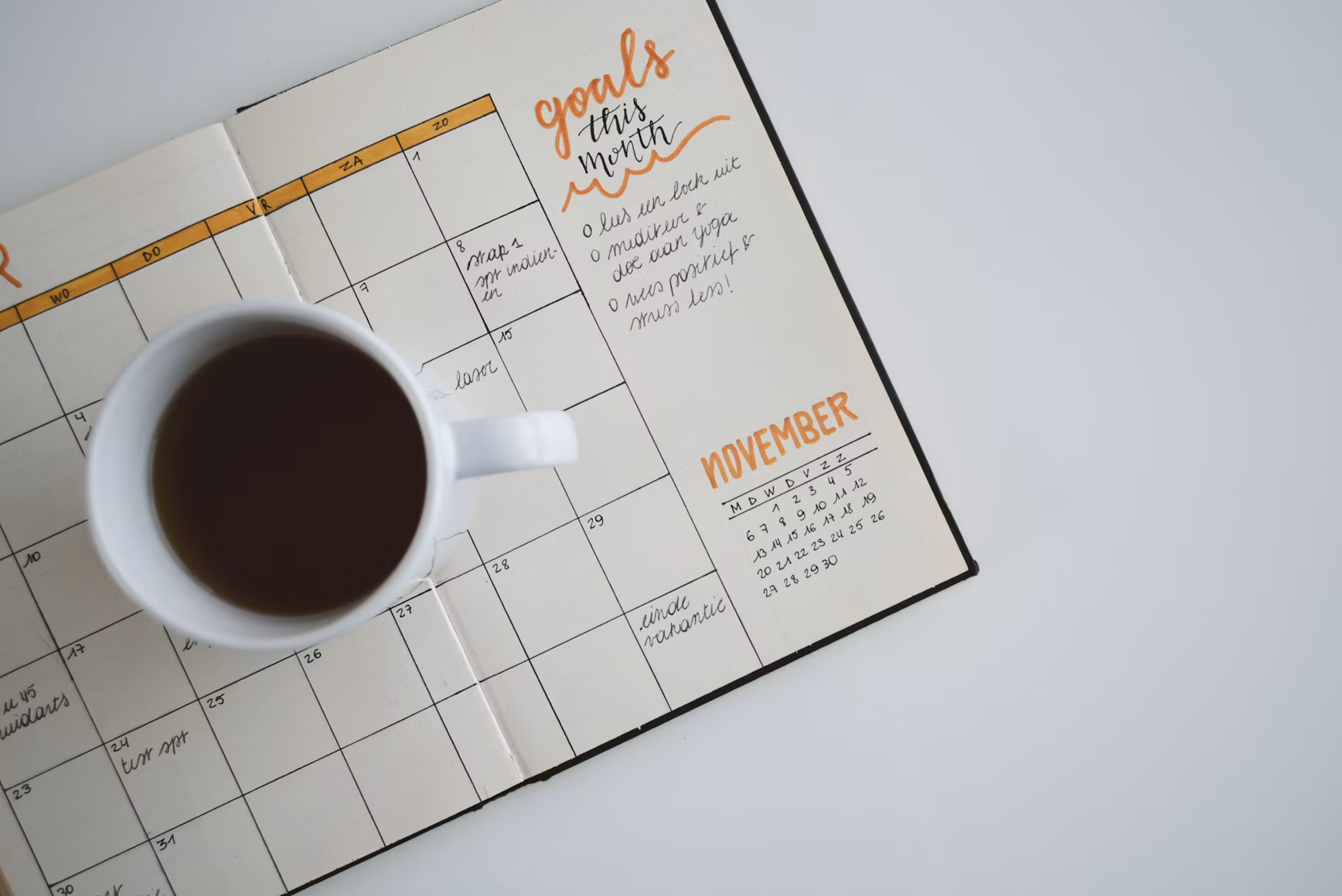 Open monthly goal planner with handwritten notes and a cup of tea on a white desk