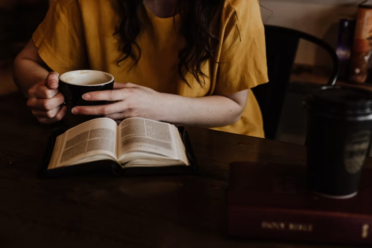 Woman holding a coffee mug beside an open book at a table.