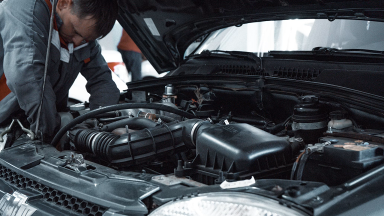 Auto mechanic inspecting a car engine under an open hood at a repair shop