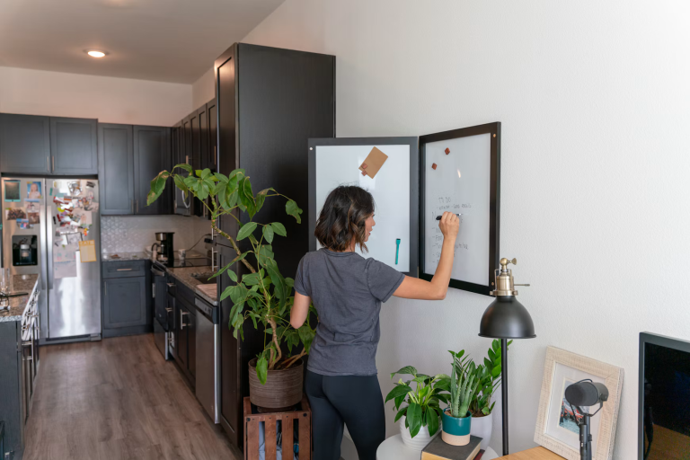 Woman writing a household task list on a whiteboard beside her kitchen