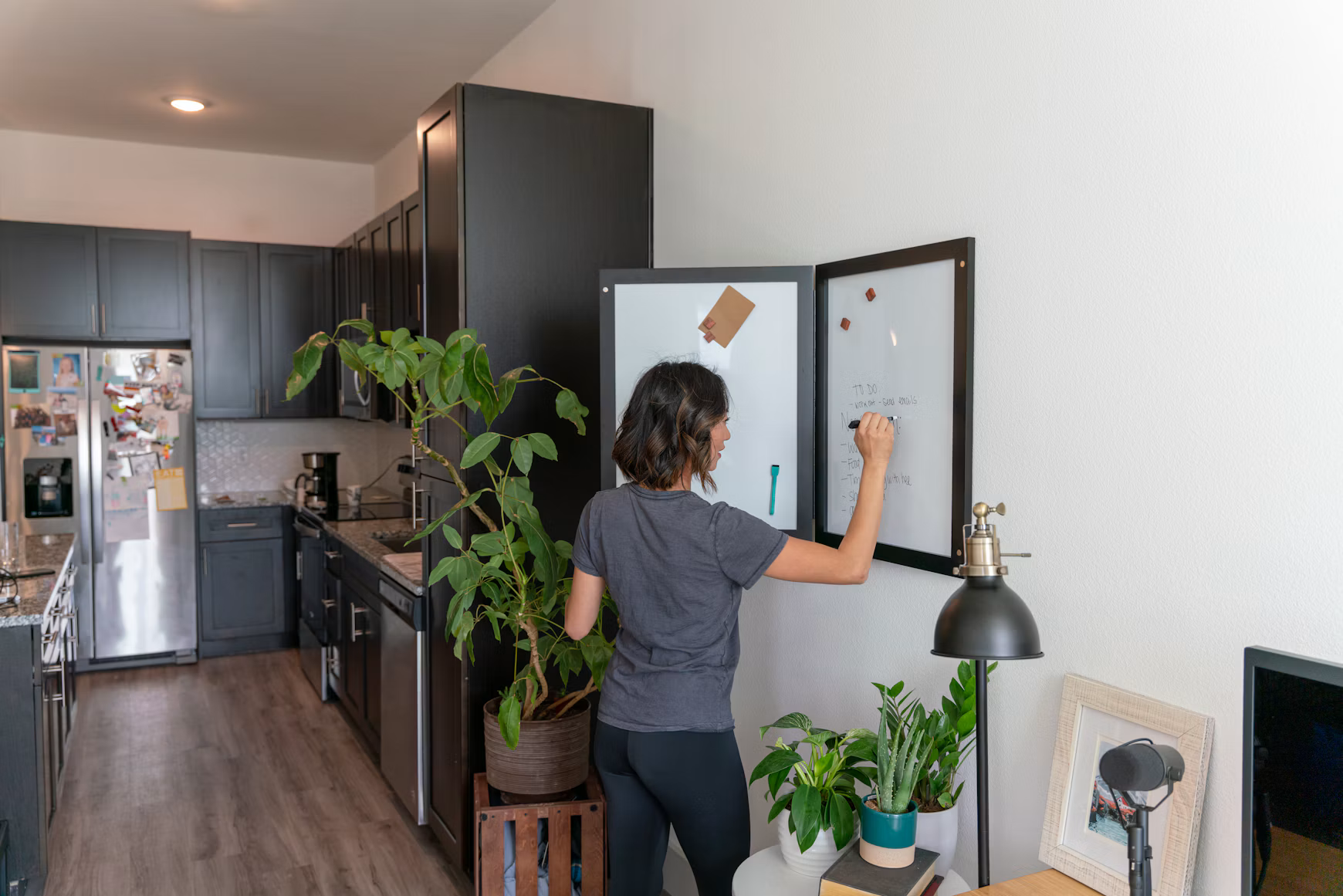 Woman writing a household task list on a whiteboard beside her kitchen
