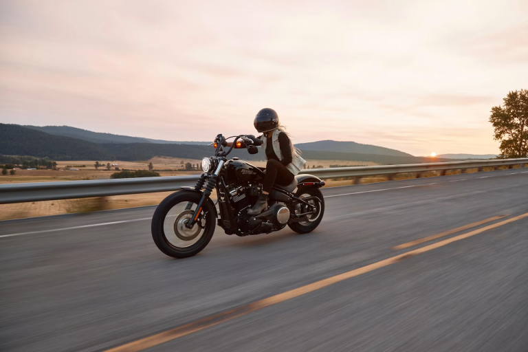 Woman wearing a helmet and protective gear while riding a motorcycle on an open road at sunset