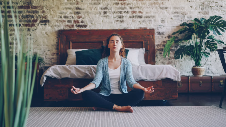 Woman meditating in a peaceful bedroom with natural wood furniture and indoor plants