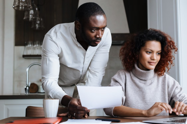 Couple reviewing paperwork and researching a home purchase on a laptop