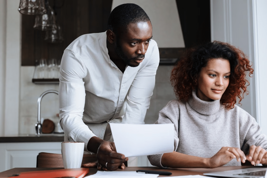 Couple reviewing paperwork and researching a home purchase on a laptop