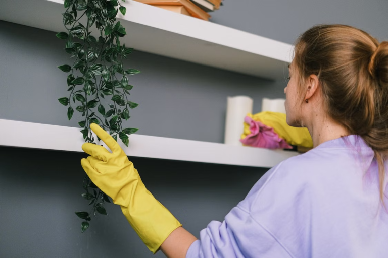 Woman wearing yellow gloves while cleaning and organizing white shelves